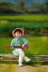 油菜花田旁弹吉他的小男孩摄影图配图