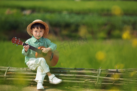 男孩子摄影照片_小宝宝手拿吉他坐在田埂上开心的笑摄影图配图