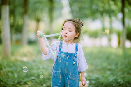 女神节手绘女孩摄影照片_儿童玩耍白天小女孩户外草坪吹泡泡摄影图配图