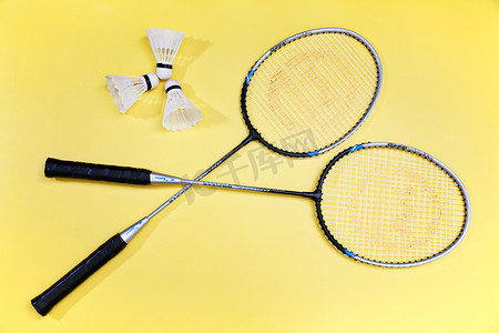 黄色背景上体育器材羽毛球拍和球静物摄影图配图