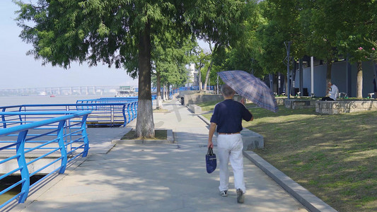 老人拎包打伞走路背影