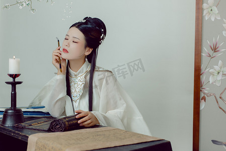 手拿毛笔伏案写字的古风美女摄影图配图