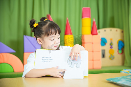 漂亮女孩理头发摄影照片_儿童教育白天可爱女孩室内读书摄影图配图