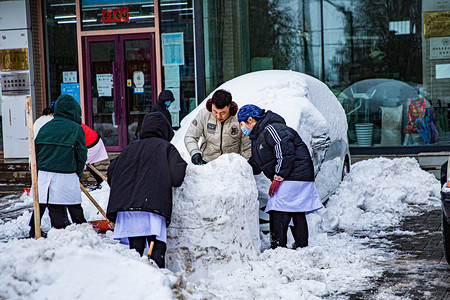辽宁雪摄影照片_冬日大雪百年一遇三五人街道堆雪人摄影图配图