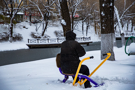 东北雪摄影照片_东北大雪百年一遇大雪老人老人健身器材静坐摄影图配图