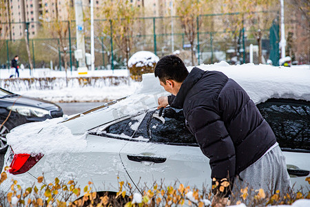 东北花色摄影照片_东北大雪立冬冬天男子铲汽车玻璃上的积雪摄影图配图