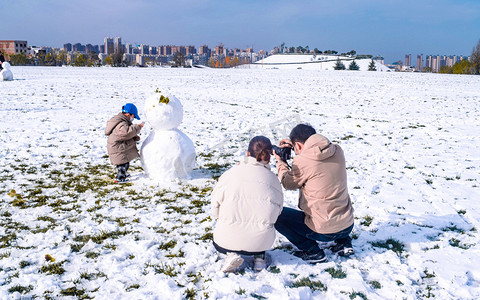 雪天摄影照片_堆雪人的一家人早晨人物雪景静止摄影图配图