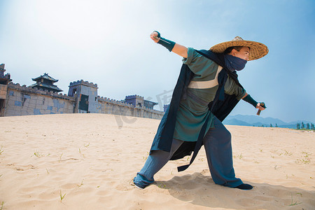 武侠人物古风摄影照片_武侠白天穿着披风的侠客户外荒漠拔剑摄影图配图