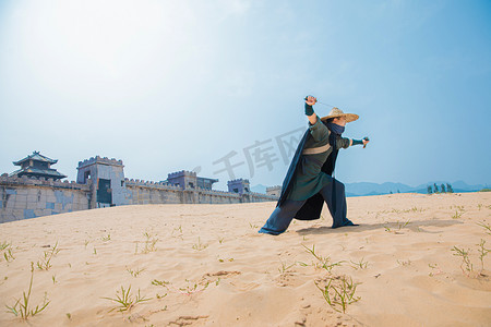 武侠人物摄影照片_古风武侠白天穿着黑色披风的侠客荒漠拔剑摄影图配图