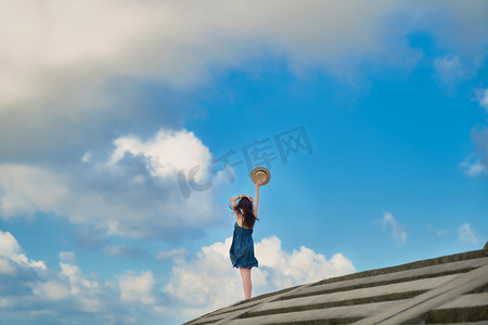海岛夏季女生蓝天白云迎风举帽子摄影图配图