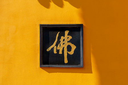 挂着书法的墙摄影照片_南京鸡鸣寺黄色山墙上的佛字摄影图配图