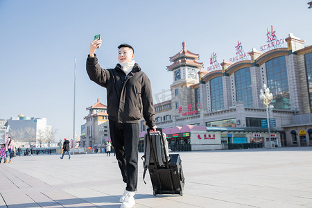 春运白天拉着行李的帅哥火车站自拍视频通话摄影图配图