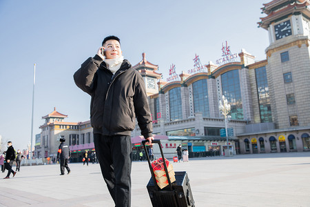 春运白天拉着行李箱的帅哥火车站打电话摄影图配图