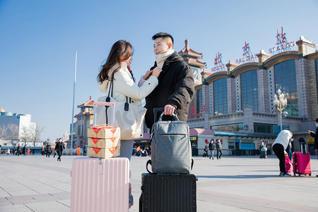 男士形象摄影照片_春运白天拉着行李箱的年轻情侣火车站整理衣服摄影图配图