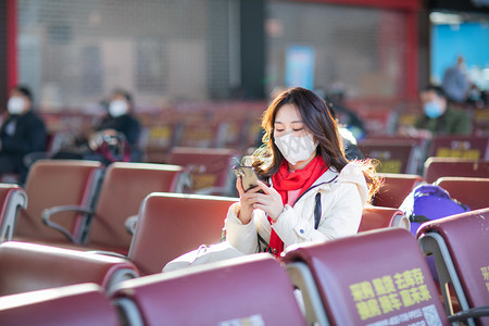 春运等车白天戴着口罩的美女候车室玩手机摄影图配图