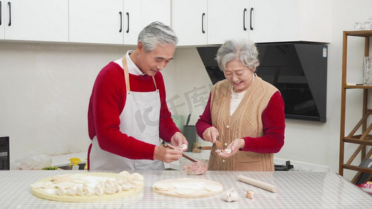 在厨房包饺子的红毛衣老年人夫妻