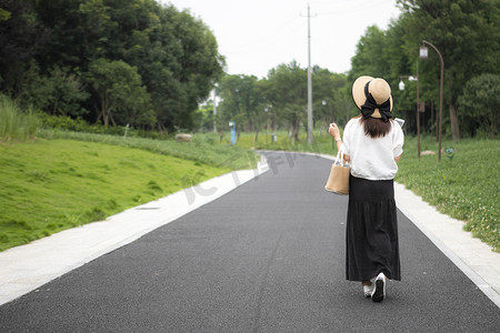 女孩走路摄影照片_公园里走路的女性背影摄影图配图