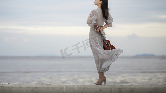 海边拿吉他的女子摄影图配图