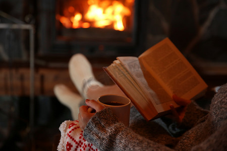 黑暗的背景摄影照片_休息与杯喝些热饮料和本书靠近壁炉旁的女人