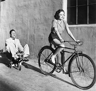 一辆自行车骑着玩具三轮车拉一个成年的男人的女人