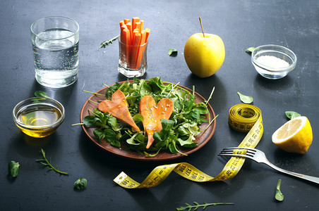 Food摄影照片_Concept diet food. Salad with arugula, leaf mash and carrots on a dark background. Vegetarian healthy dish that promotes weight loss.