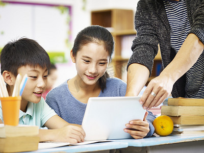 人像摄影照片_亚洲的小学生使用数字平板电脑在教室里