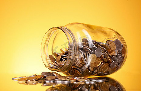 硬币从钱罐子里洒上黄色的背景。乌克兰语