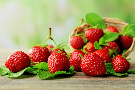 成熟的草莓，叶长在柳条篮中，背景模糊，木制桌子上