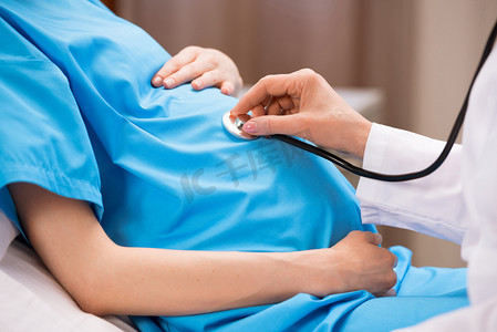 怀孕的人摄影照片_用听诊器在给孕妇听诊的医生