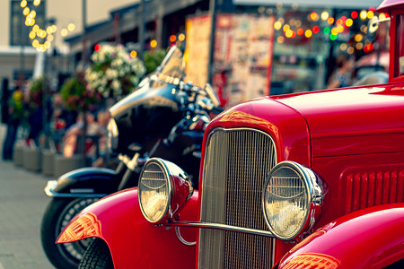古董车摄影照片_在现代摩托车的背景下，一辆带有彩色前灯的老式红色轿车出现在夏季街道上。拉脱维亚里加