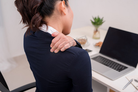 颈部疼痛摄影照片_年轻的商业人颈部疼痛。将笔记本电脑放在桌面上以手放在颈部.