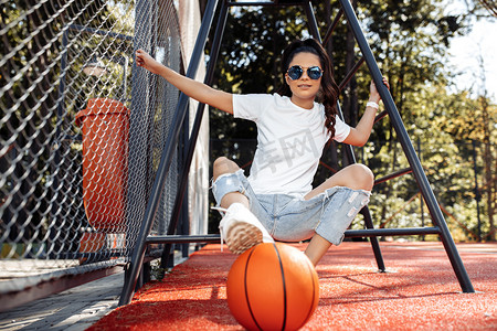 欧美健身女孩摄影照片_一位可敬的年轻女子身穿休闲的现代服装，在体育场打篮球.
