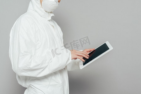 保护屏幕摄影照片_身着危险物品套装、戴着口罩、手持灰色背景空白屏幕数码平板电脑的流行病学家的剪影