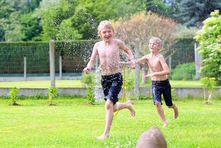 两个快乐的男孩，与浇水软管花园里玩