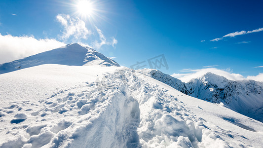 爬山山顶摄影照片_灿烂的阳光和蓝色的白雪覆盖的山顶
