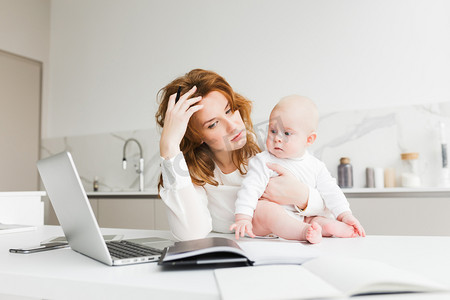 商业人物女摄影照片_商业妇女抱着她的小宝宝坐在桌子工作