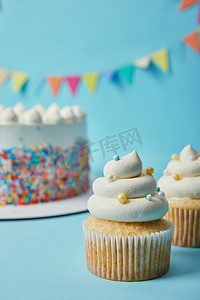 会议背景蓝色摄影照片_美味的纸杯蛋糕与糖洒在蓝色背景与蛋糕和彩带