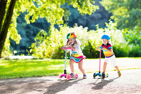 体育家庭摄影照片_孩子们骑着滑板车中夏公园.