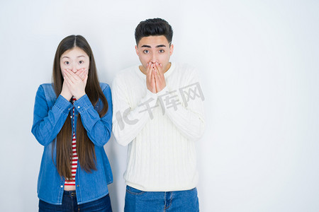 害羞的手拿雨伞摄影照片_Beautiful young asian couple over white isolated background shocked covering mouth with hands for mistake. Secret concept.