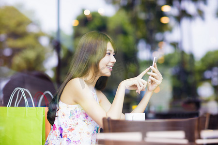 微笑的看着智能手机在咖啡屋的年轻女士