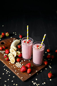 水果和牛奶摄影照片_香蕉和草莓冰沙在黑色背景上的玻璃