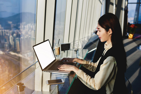 年轻的亚裔女子，在舒适的咖啡厅，与城市空间景观的现代电脑前工作时