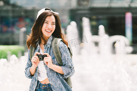 旅游业摄影照片_年轻漂亮的亚洲背包旅行女子使用数码相机和微笑, 看着复制空间。旅行旅行生活方式, 世界旅行探险家或亚洲夏天旅游业概念