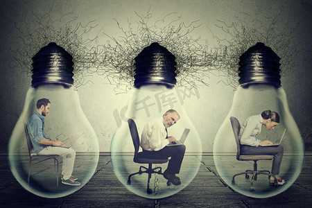 信息共享摄影照片_Company employees sitting in row inside electric lamp light bulb using laptop 