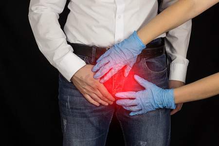 一个穿牛仔裤和白衬衫的男人正抱着腹股沟戴着医疗手套的女人手里握着一个男人的腹股沟黑色背景前列腺炎