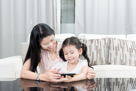 父母玩游戏摄影照片_亚洲母亲和女儿玩数字平板电脑在家里