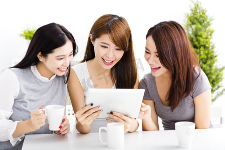 三个快乐的年轻女子看在客厅里的平板电脑
