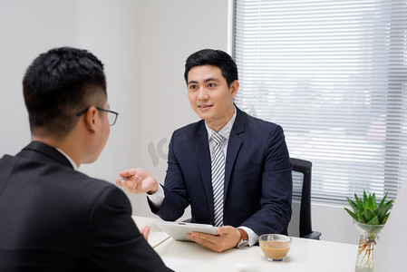 商务会议。两个做生意的人坐在对方的前面在办公室里, 而讨论的东西