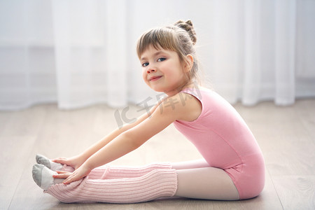 运动风格摄影照片_可爱的小女孩在粉红色紧身连衣裤在舞蹈工作室制作新芭蕾运动