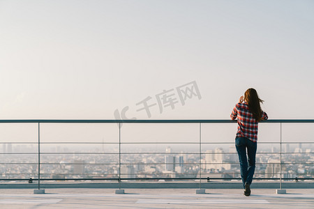 副本空间摄影照片_在夕阳与副本空间、 通信或寂寞的人概念在屋顶使用移动电话的女人